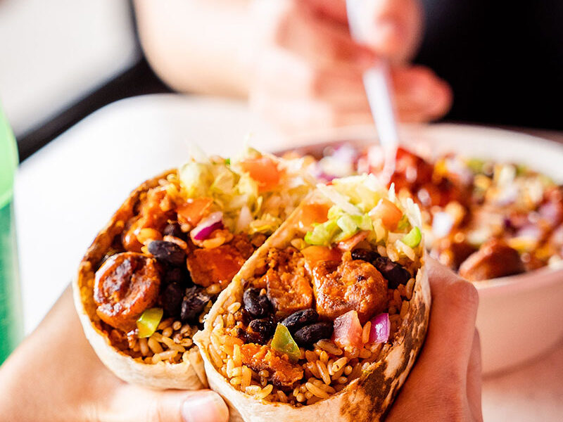 close up photo of a person holding a halved burrito with two hands at a dining table