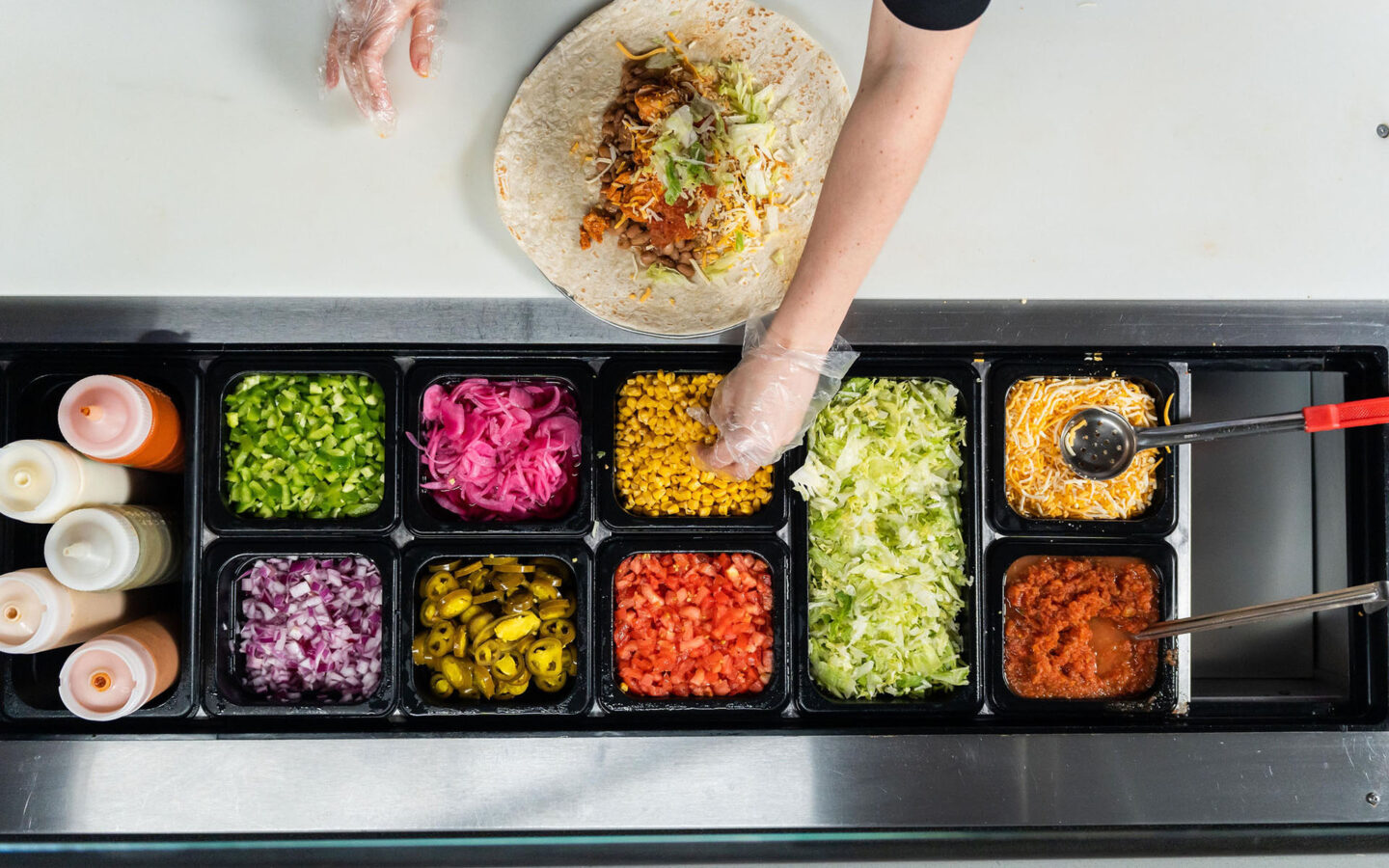 overhead photo of a person reaching for an ingredient while making a burrito