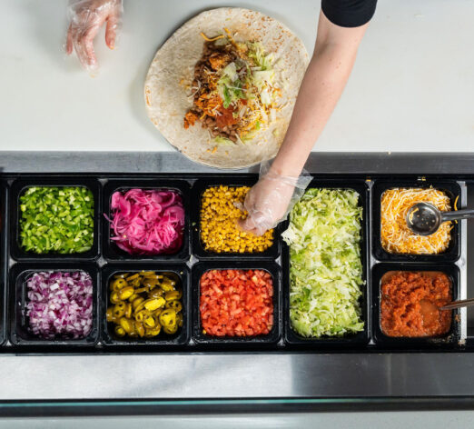 overhead photo of a person reaching for an ingredient while making a burrito