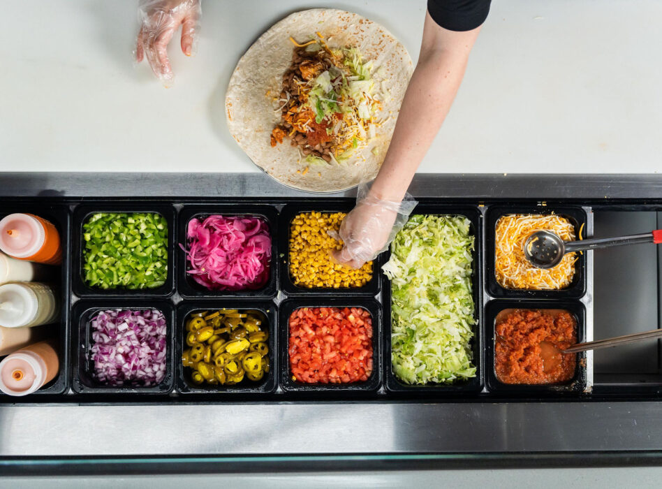 overhead photo of a person reaching for an ingredient while making a burrito