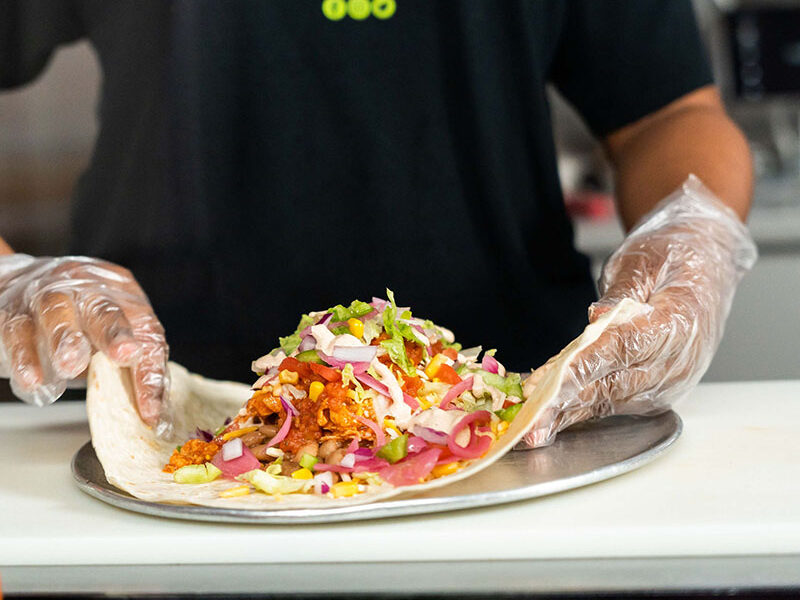 an employee wearing a black shirt and gloves making a burrito