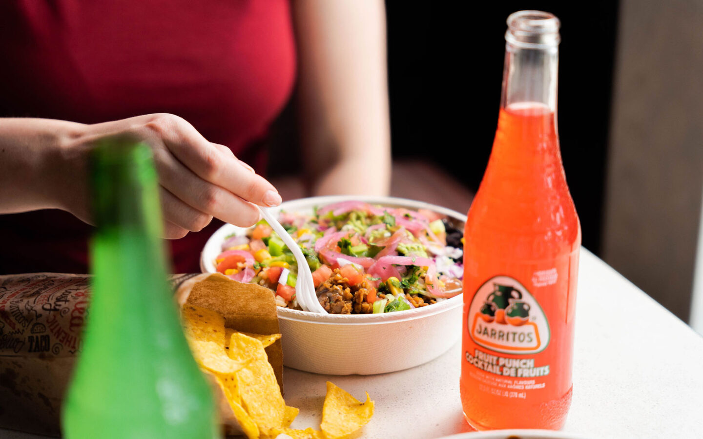 a woman eating a burrito bowl with a jarritos soda
