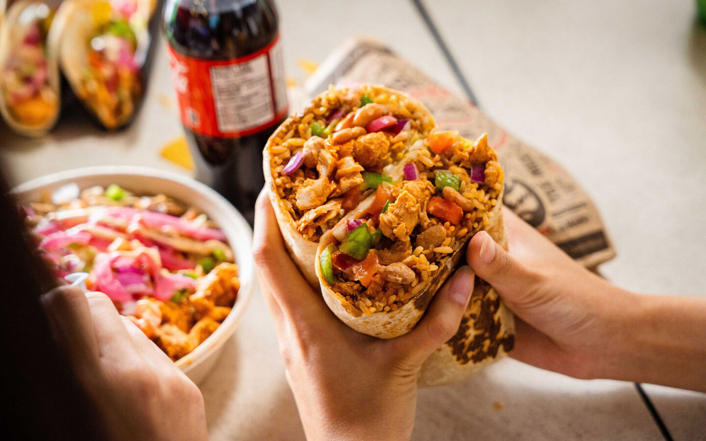 two hands holding a burrito cut in half and stacked on top of each other