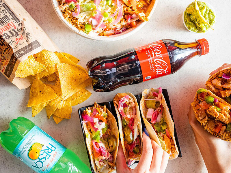 overhead photo of three people eating tacos, burritos and a burrito bowl