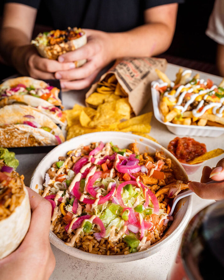 two people sitting and eating a burrito bowl, burritos, fries supreme and tacos