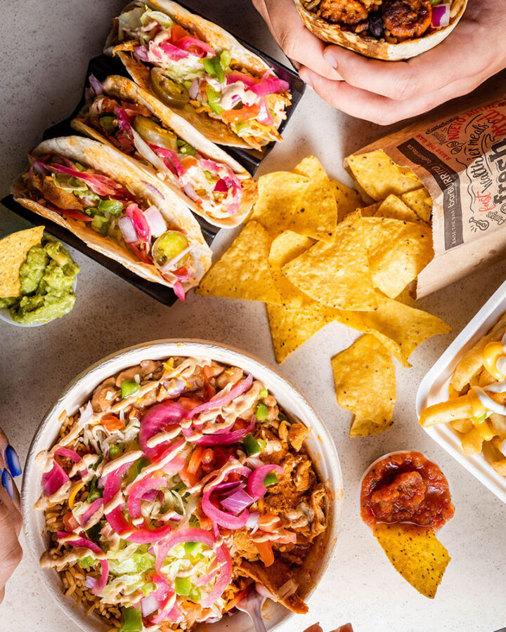 overhead photo of two people eating a burrito bowl, chips and salsa, tacos and a burrito